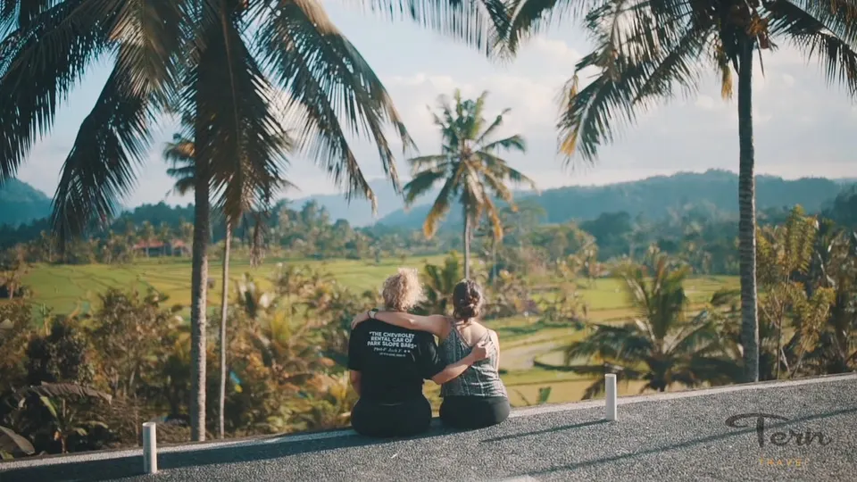 Two travellers sitting under palms above Bali rice terraces