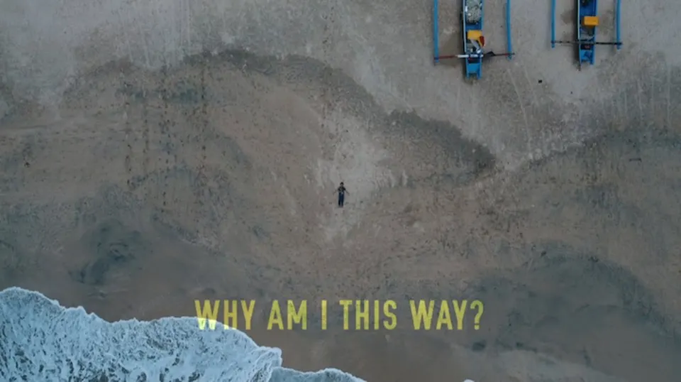 Aerial shot of a lone figure lying on a dark volcanic beach